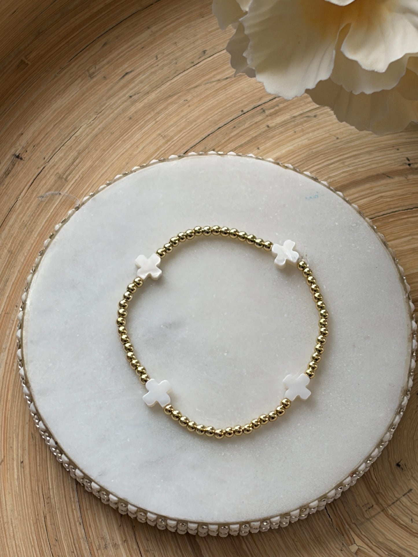 Bracelet with gold and white cross beads on a marble plate with a wooden background