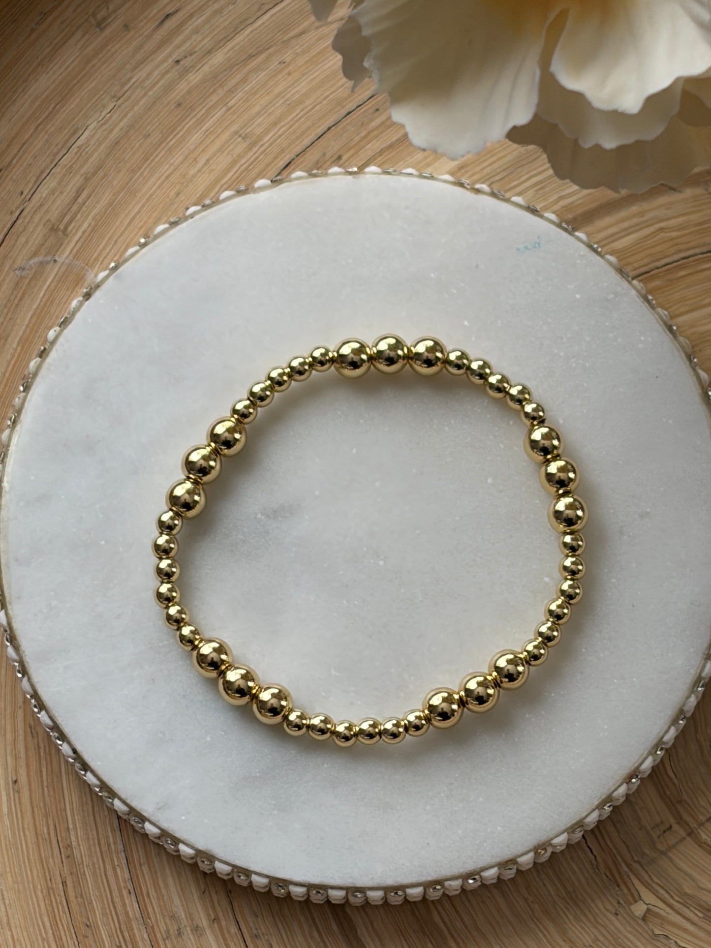Gold beaded bracelet on a marble surface with a light wooden background