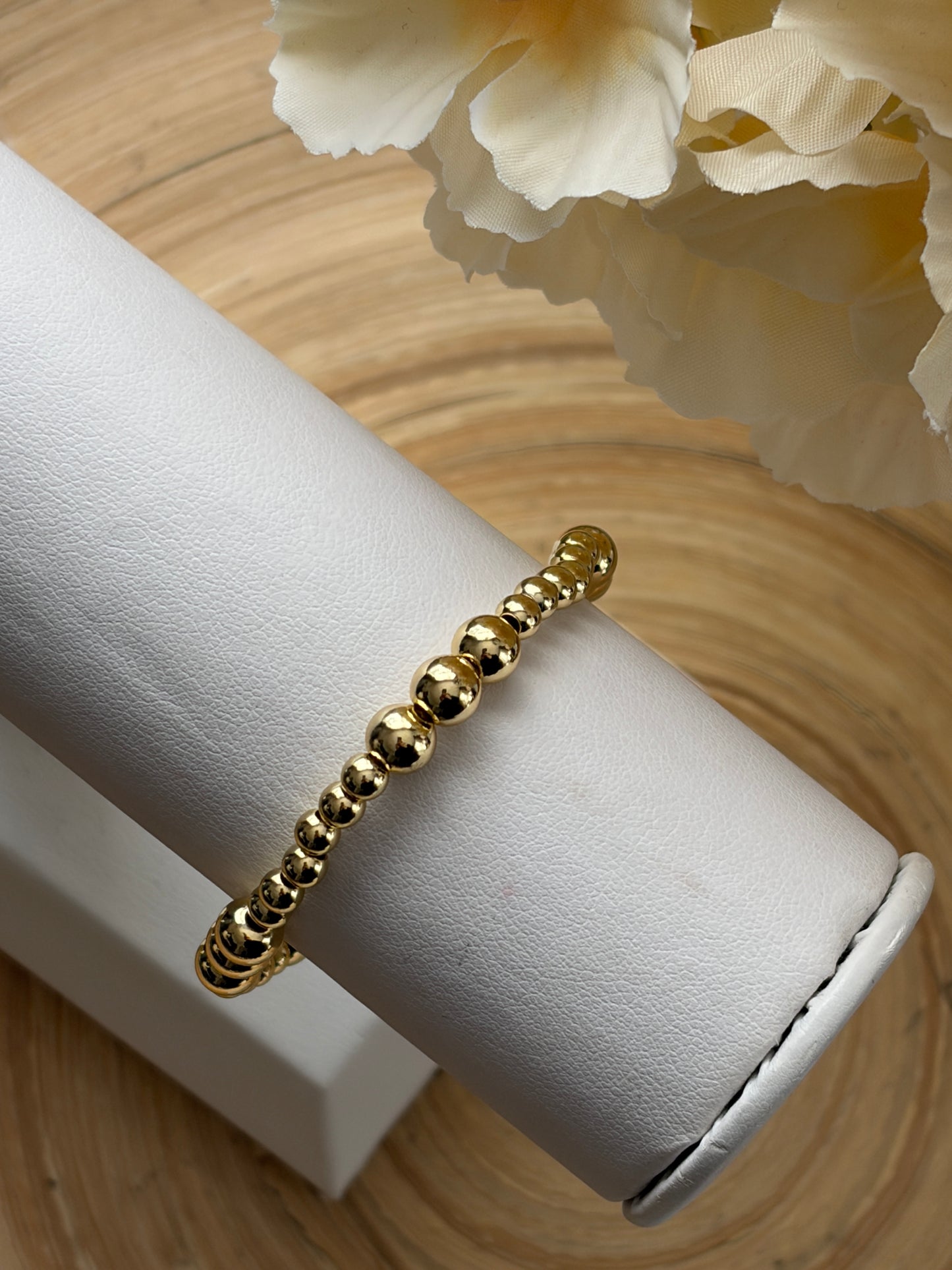 Gold bracelet on a white jewelry display with a floral background