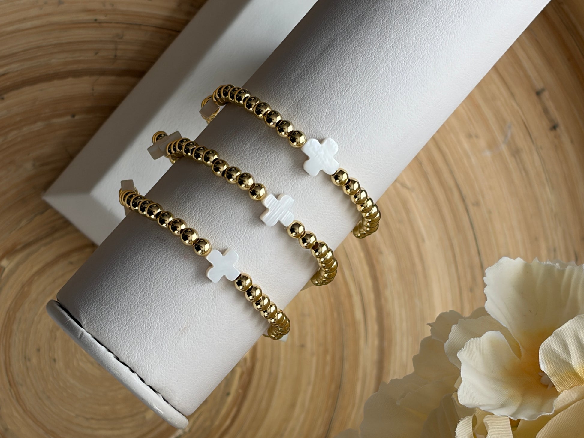 Gold bracelet with white crosses on a white cylindrical stand against a wooden background