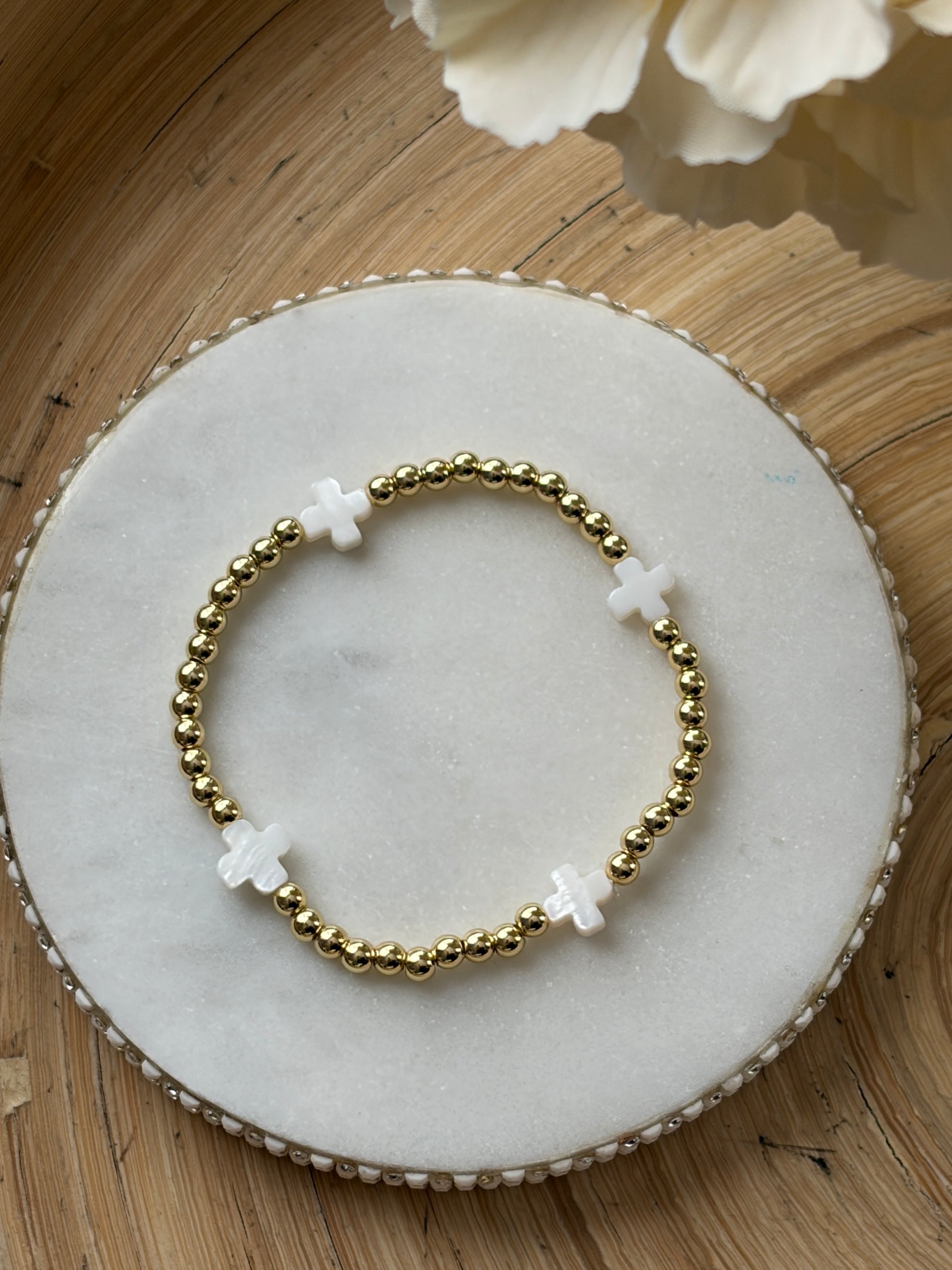 Gold beaded bracelet with white beads on a marble coaster with flowers in the background