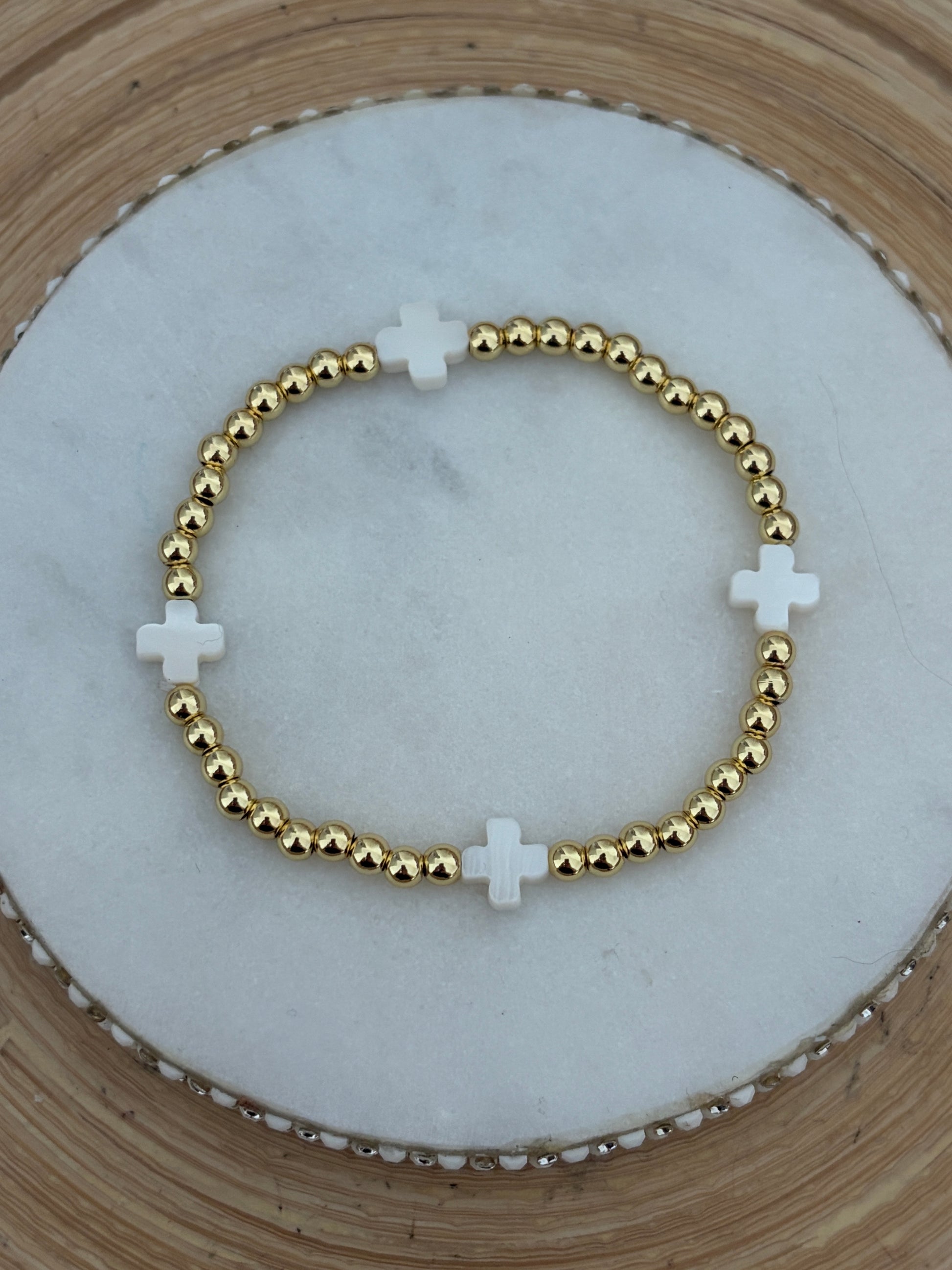 Gold beaded bracelet with white crosses on a marble surface